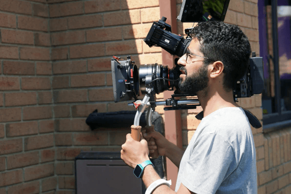 Cinematographer frames man against brick wall sunlight.